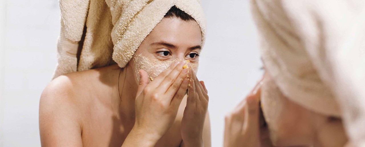Young woman exfoliating her face in the mirror