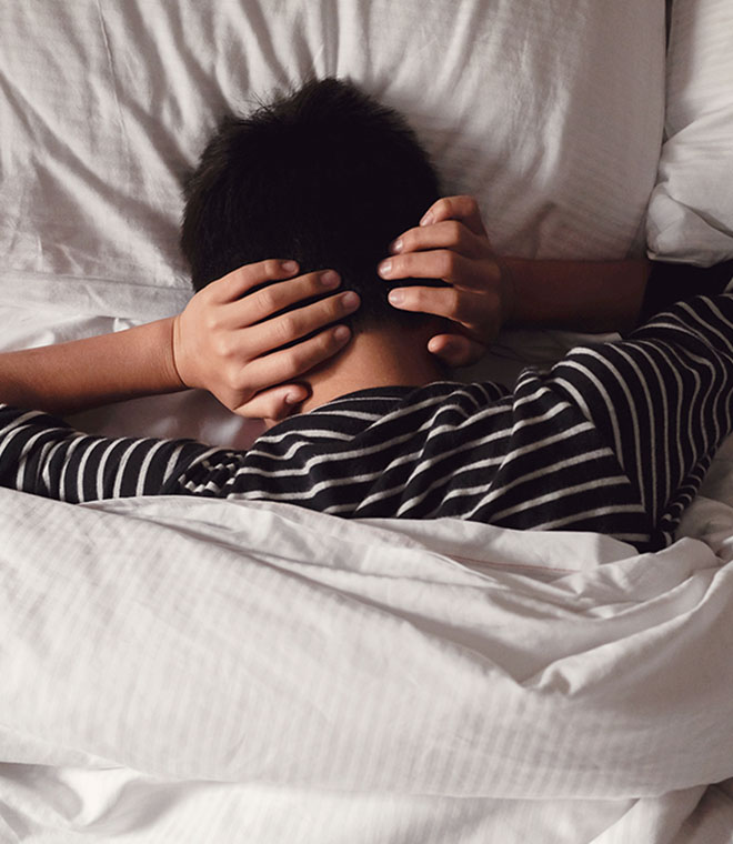 Person laying in bed holding their head