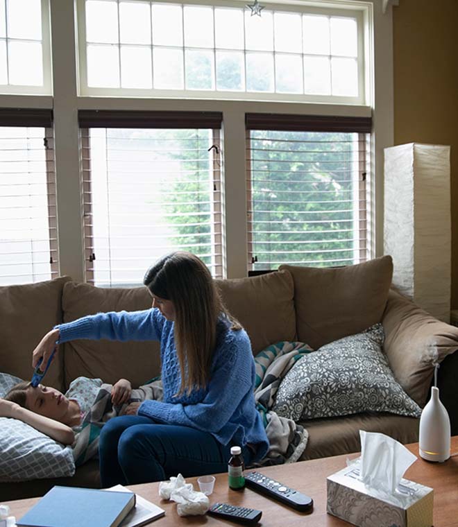 White woman checking forehead temperature of child laying on couch