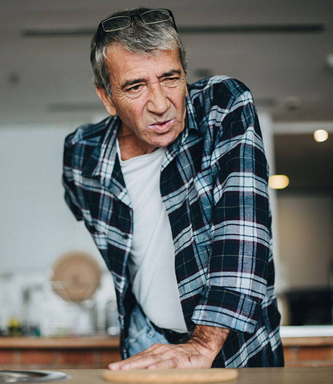 Older white man leaning over and holding his back