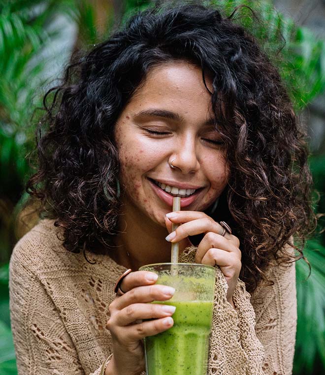 Woman with curly hair drinking a green drink