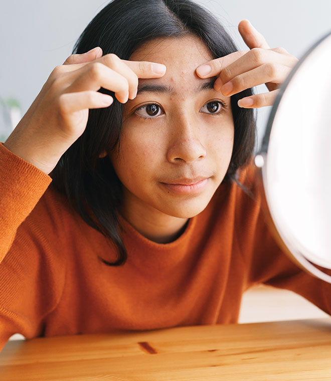 Teenage girl picking at her forehead in the mirror