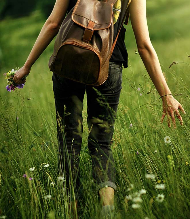 Woman walking through a field of long grass and wild flowers